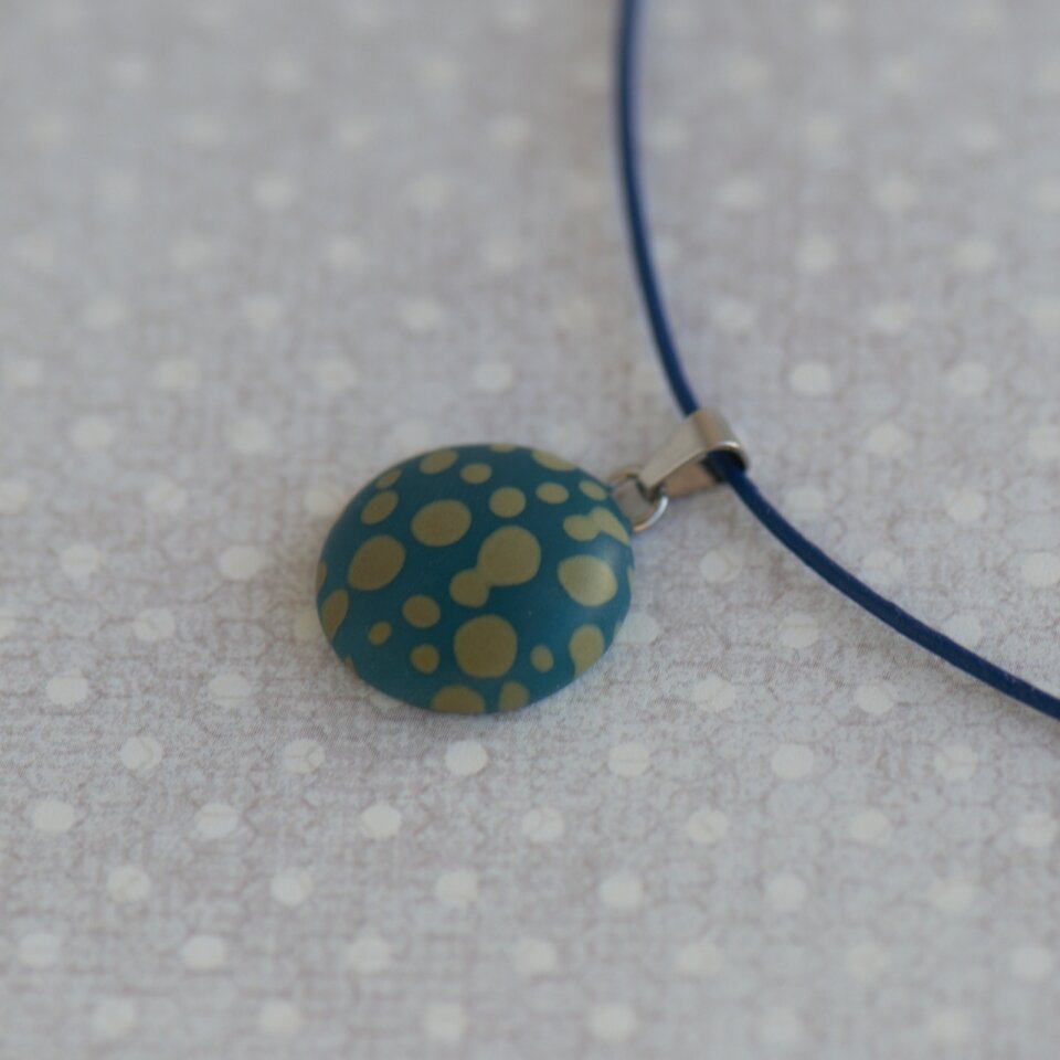 Rankų darbo pakabukas su taškeliais mėlynai žalios spalvos fone