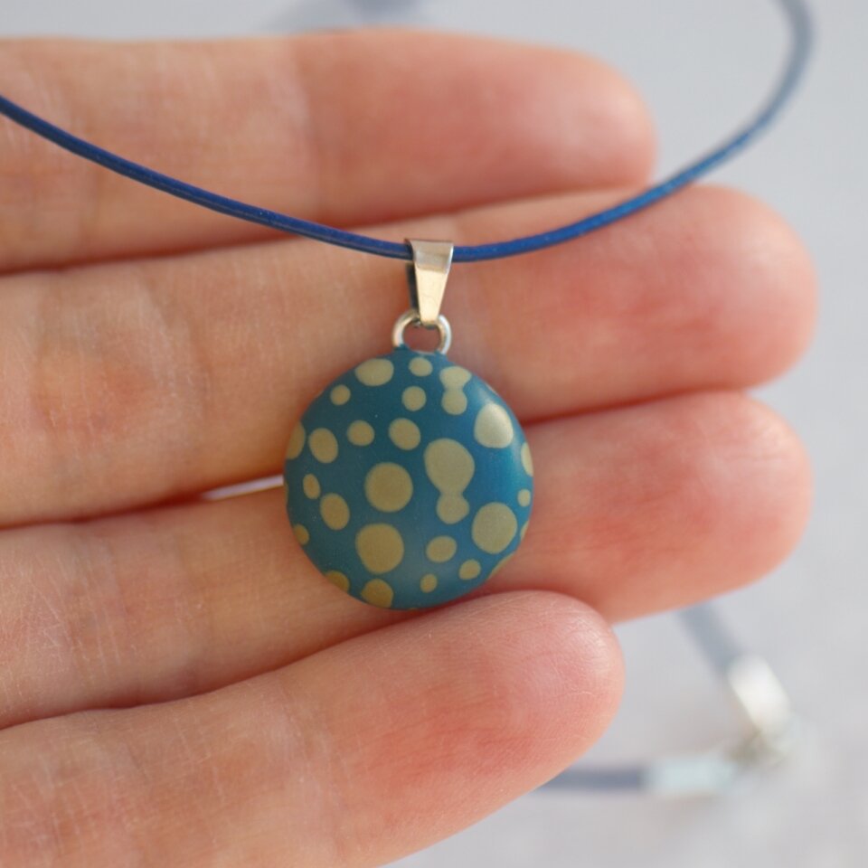 Rankų darbo pakabukas su taškeliais mėlynai žalios spalvos fone